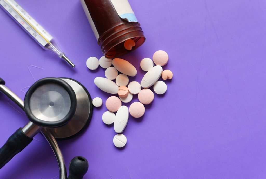 An image of a Stethoscope, a pill bottle, some pills and a syringe