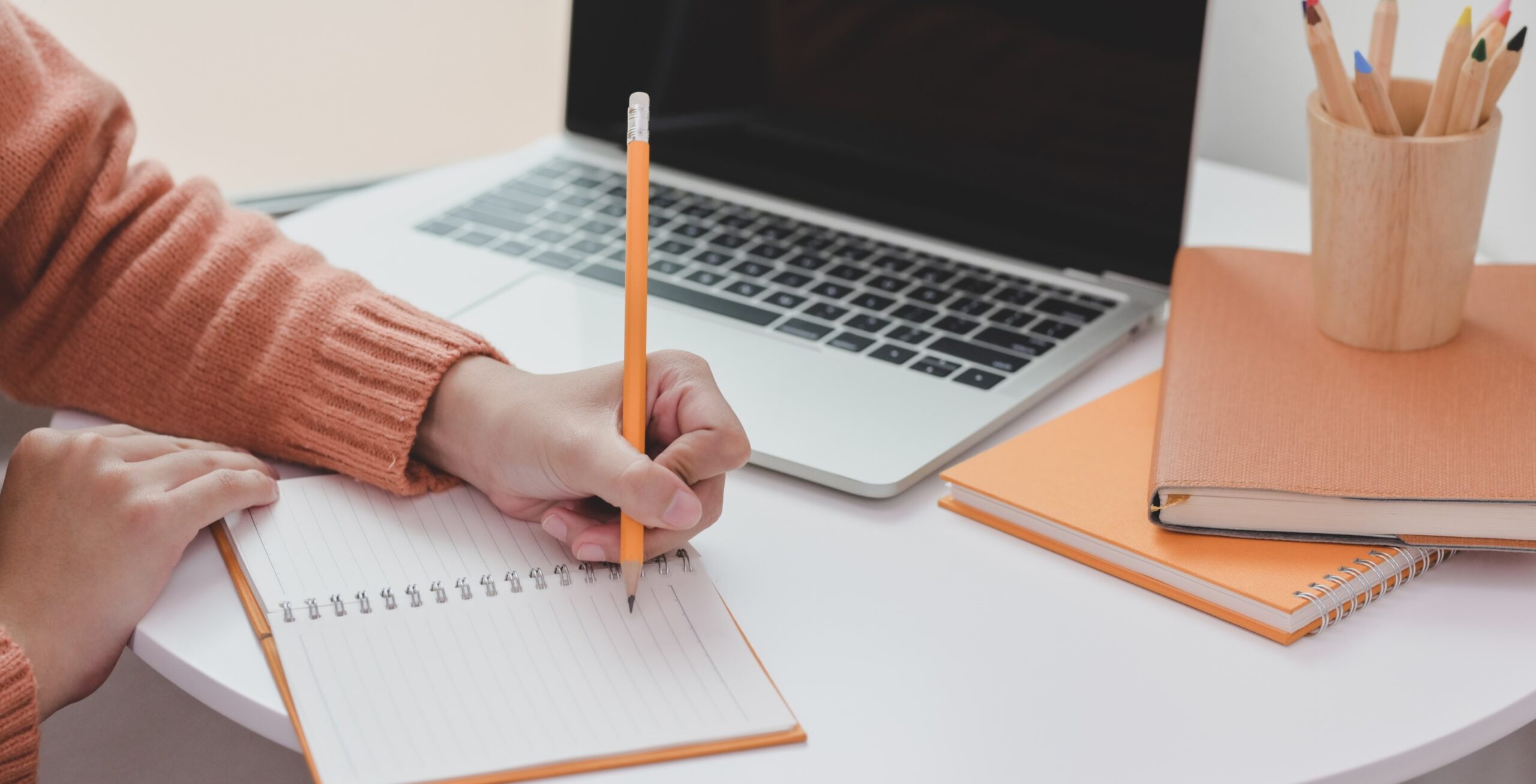 Person writing in a notepad by a laptop