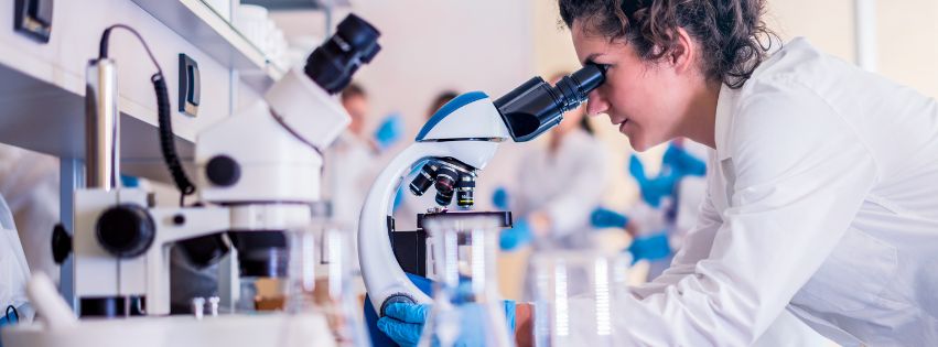 A scientist looking down a microscope in a lab